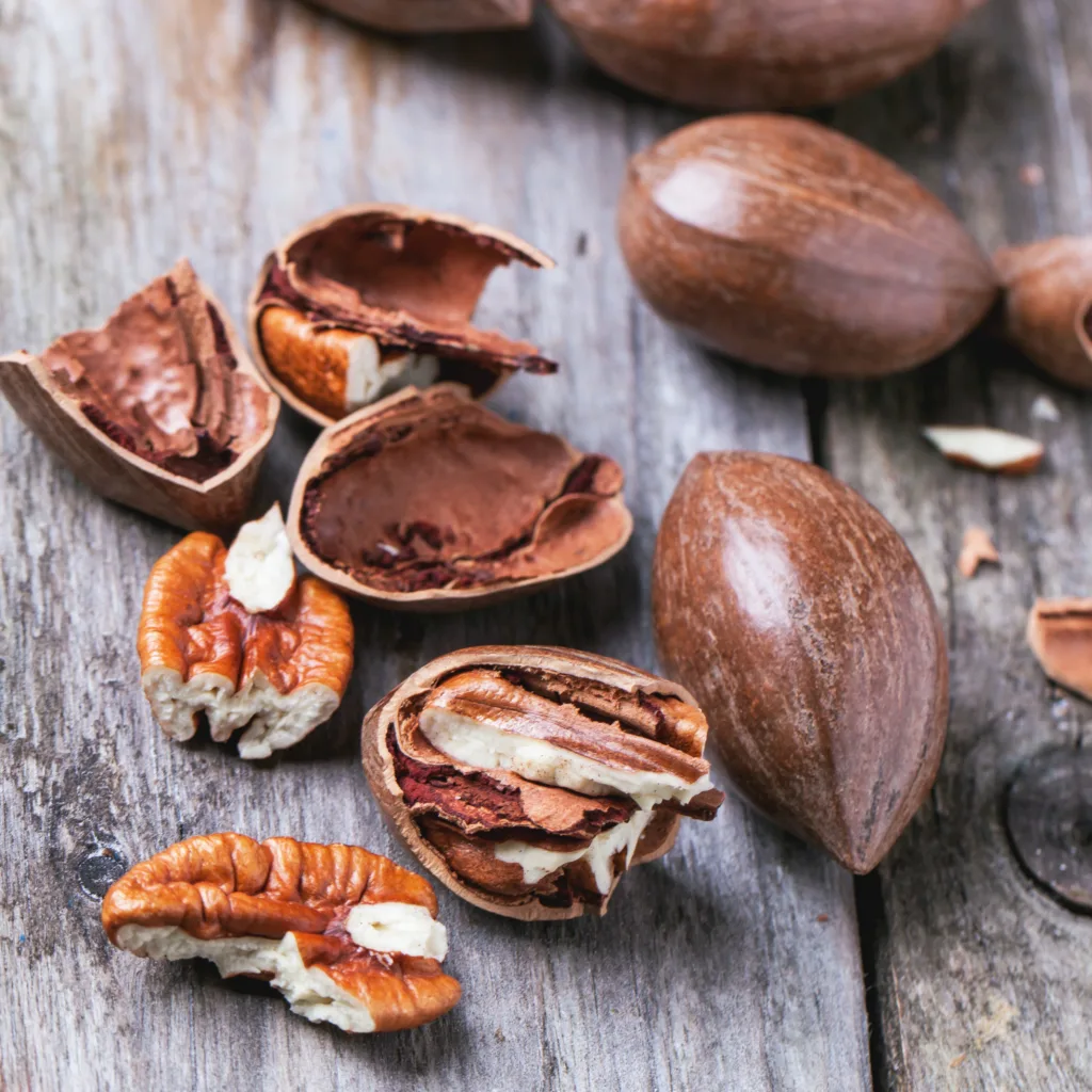 Whole and chopped pecan nuts on old wooden table.